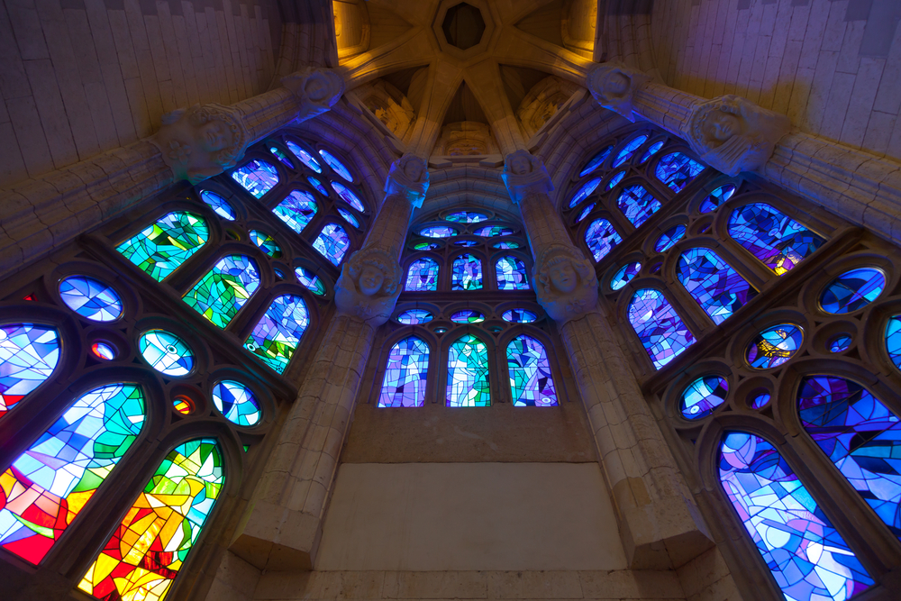 Stained glass windows rising to a vaulted stone ceiling inside a cathedral