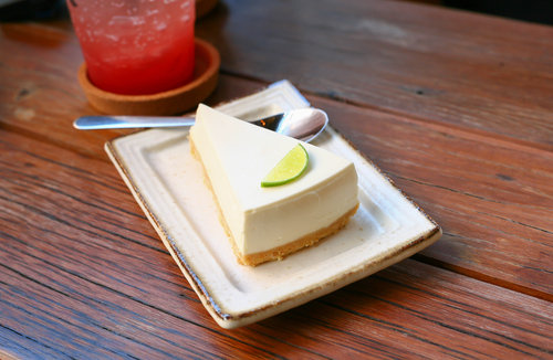 Slice of cheesecake topped with a lime wedge on a wooden table