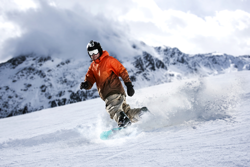 Snowboarder in an orange jacket carving down a snowy mountain slope