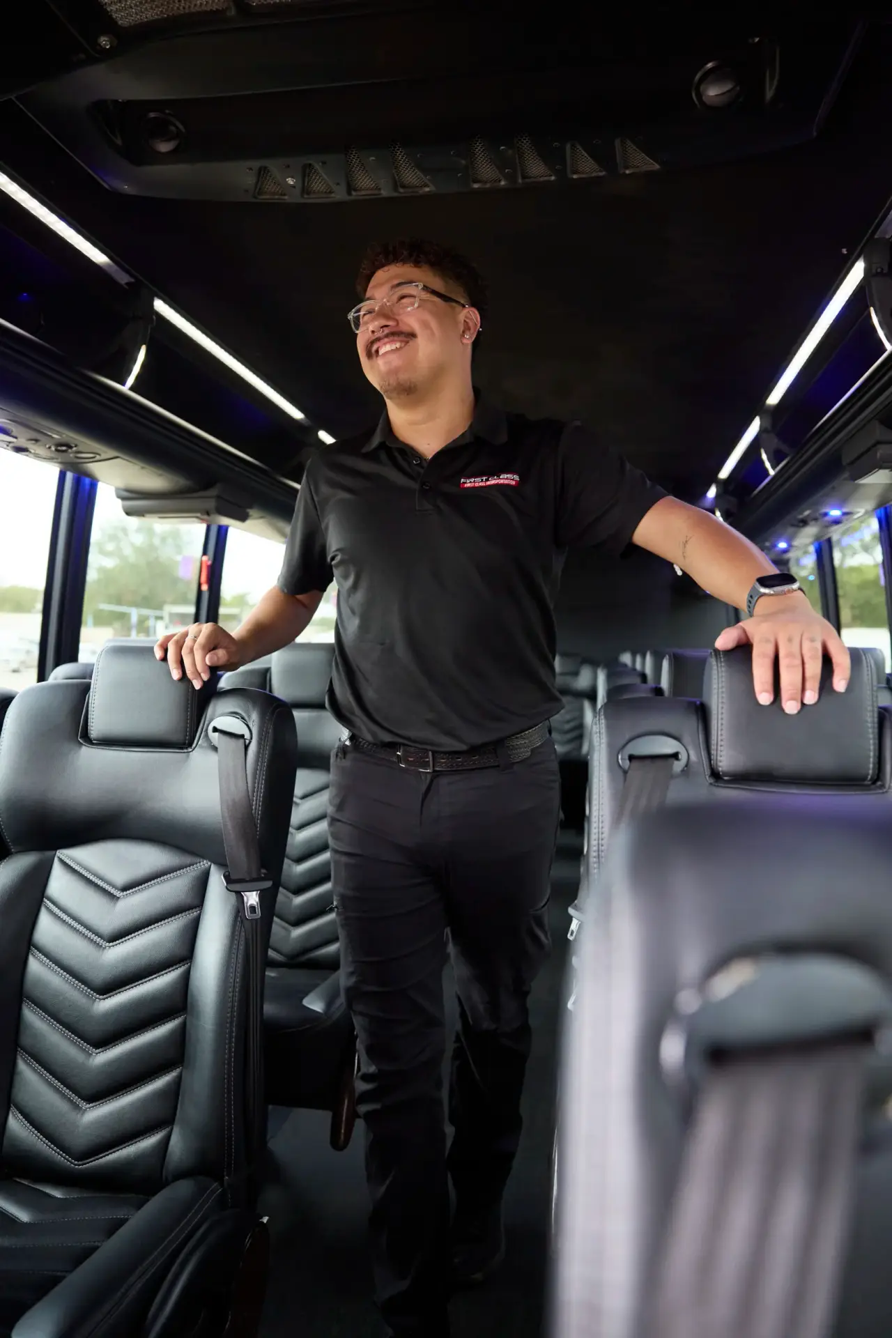 Smiling First Class Transportation team member in a company polo standing in the aisle of a motorcoach