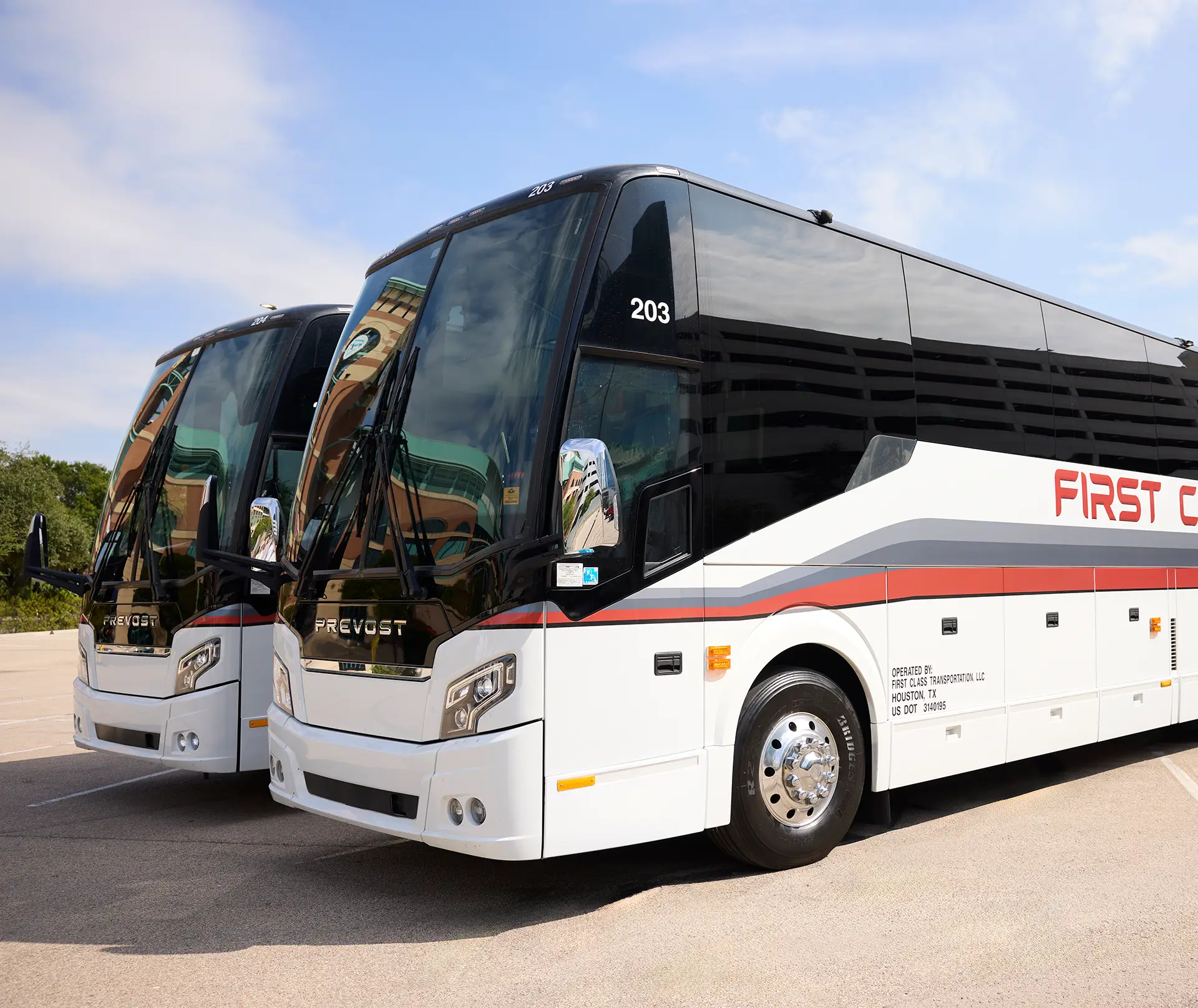 Two white First Class Transportation Prevost motorcoaches parked side by side