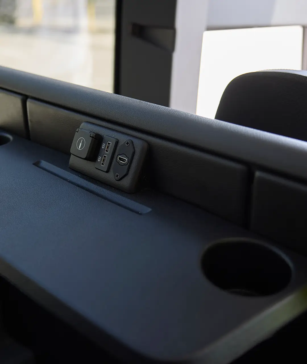 USB and HDMI charging port panel on a First Class Transportation motorcoach seat-back tray with cup holder