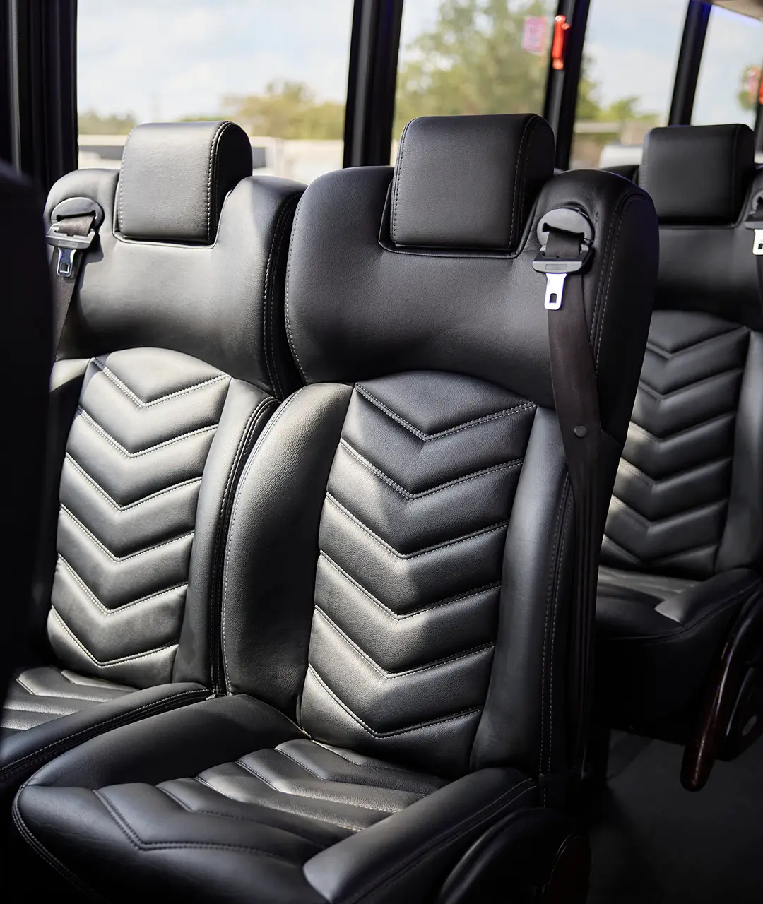 Black leather chevron-stitched passenger seats with seatbelts inside a First Class Transportation motorcoach