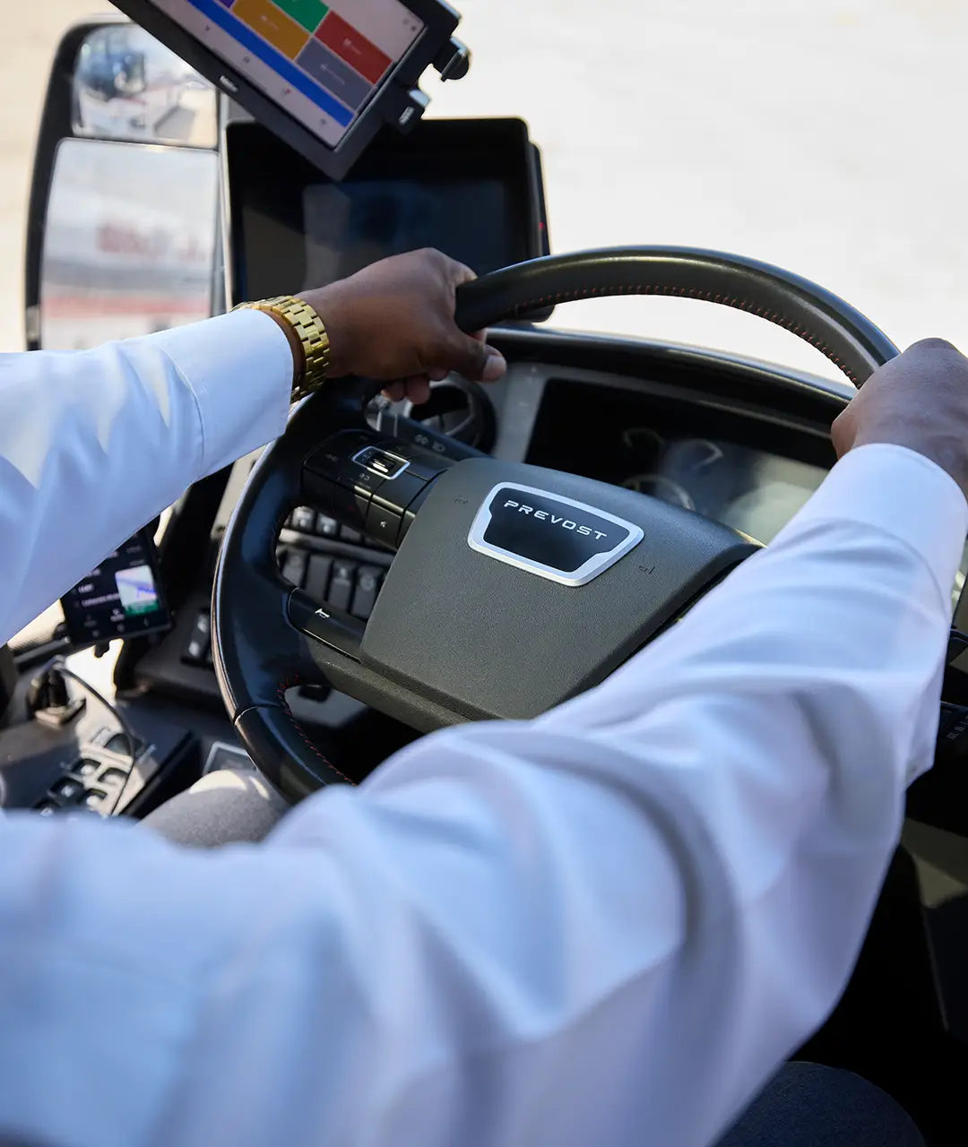 Driver's hands on the Prevost steering wheel and digital dashboard of a First Class Transportation motorcoach
