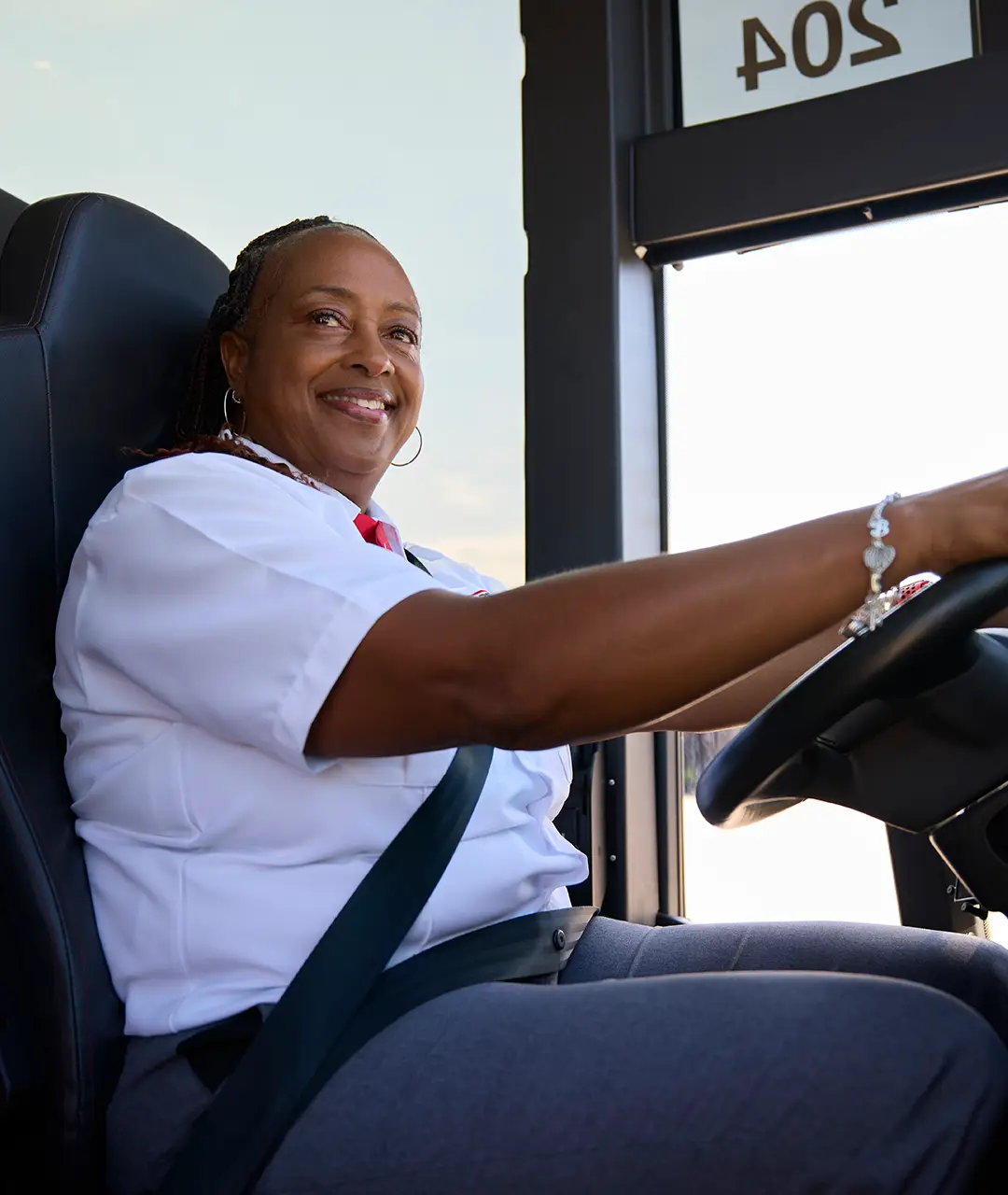 Smiling First Class Transportation driver in a white uniform shirt and red tie driving a motorcoach
