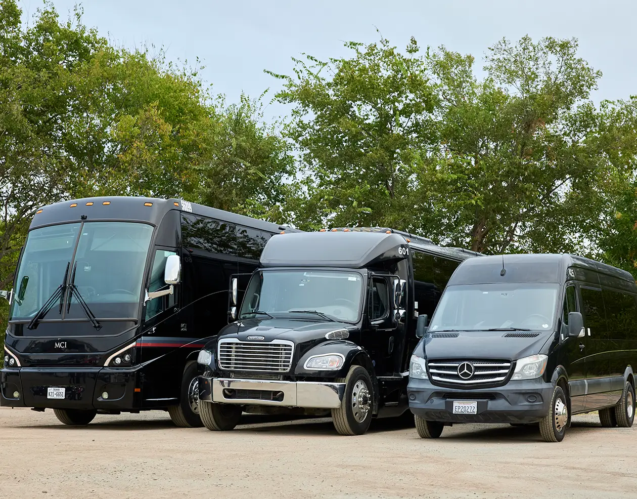 Black First Class Transportation MCI motorcoach, minibus, and Mercedes-Benz Sprinter van parked on gravel