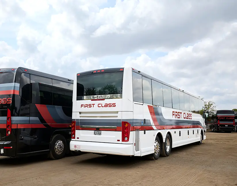 White First Class Transportation Van Hool motorcoach parked beside a black motorcoach