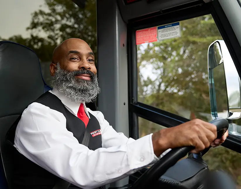 Smiling First Class Transportation driver in uniform at the wheel of a motorcoach