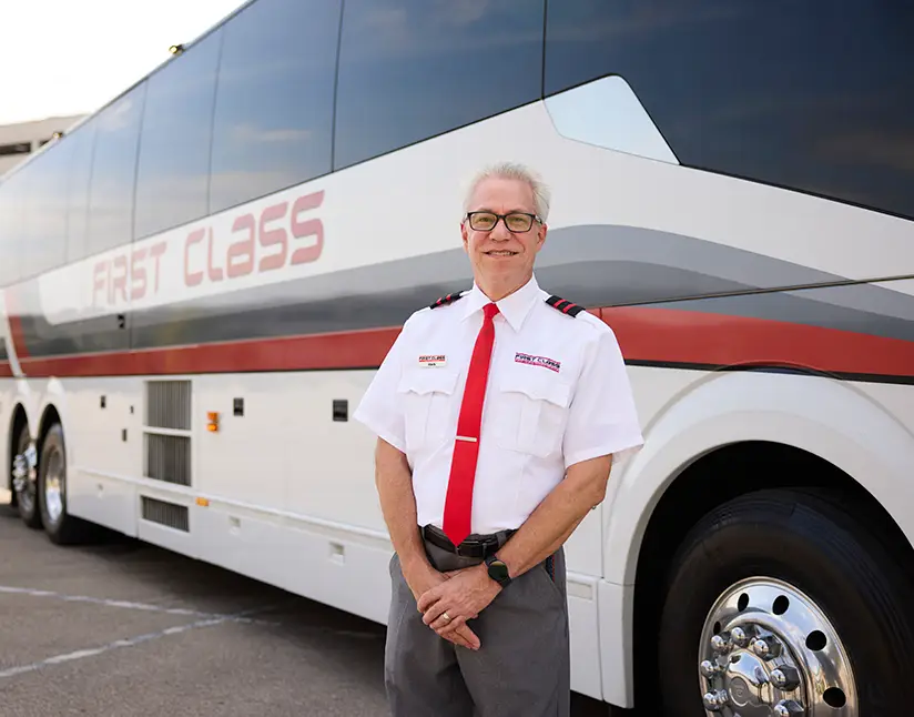 First Class Transportation driver in uniform standing beside a motorcoach