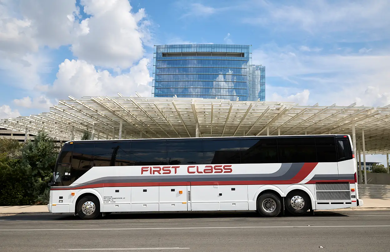 White First Class Transportation full-size motorcoach parked in front of a modern glass office building