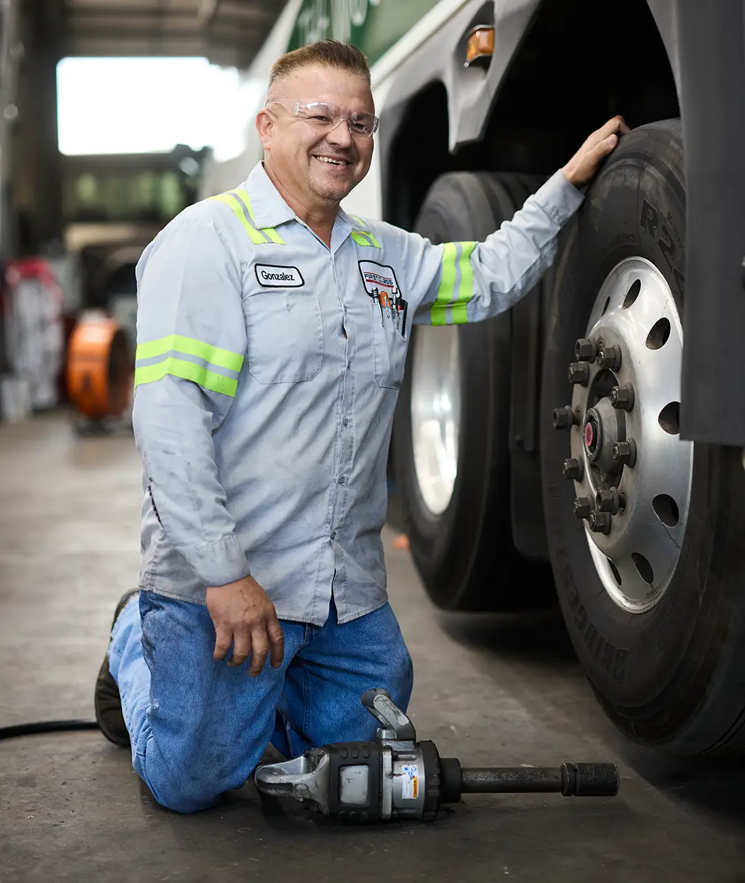 First Class Transportation technician kneeling beside a motorcoach wheel with an impact wrench in the maintenance shop