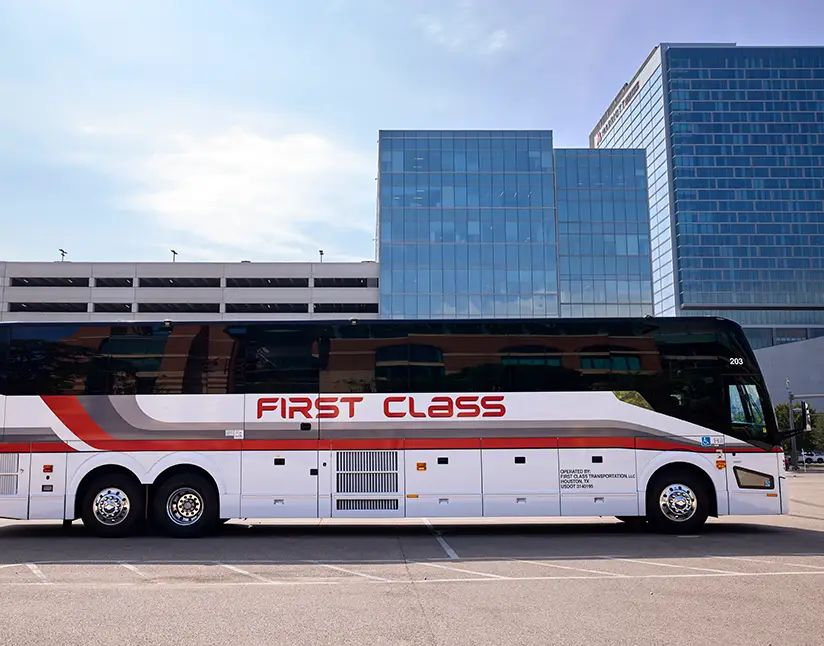 White First Class Transportation motorcoach with red First Class lettering parked outside an office building
