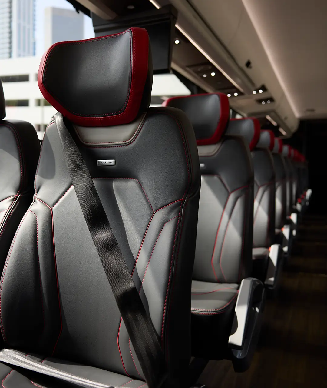 Rows of black leather seats with red trim inside a First Class Transportation Prevost motorcoach
