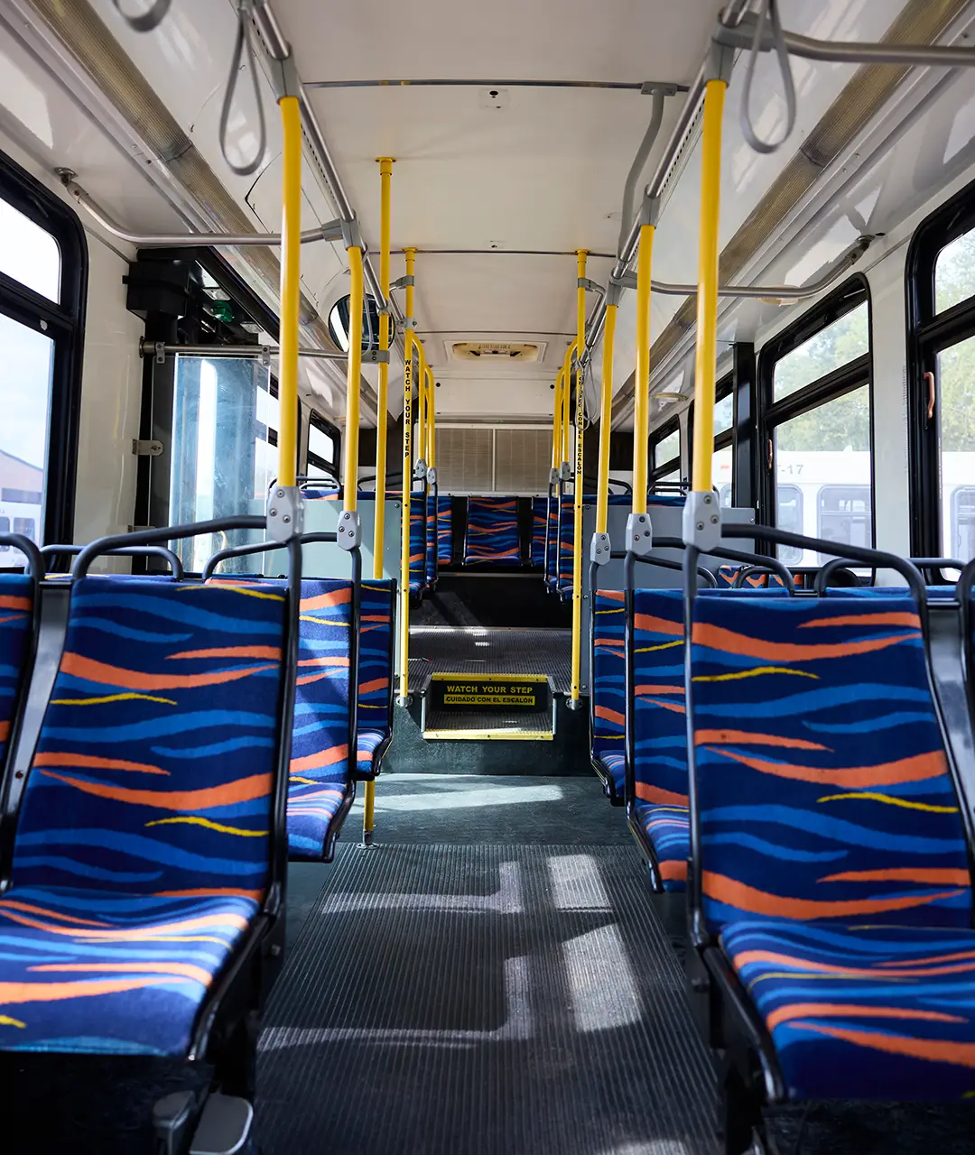 Interior of a First Class Transportation transit bus with blue patterned seats and yellow grab poles