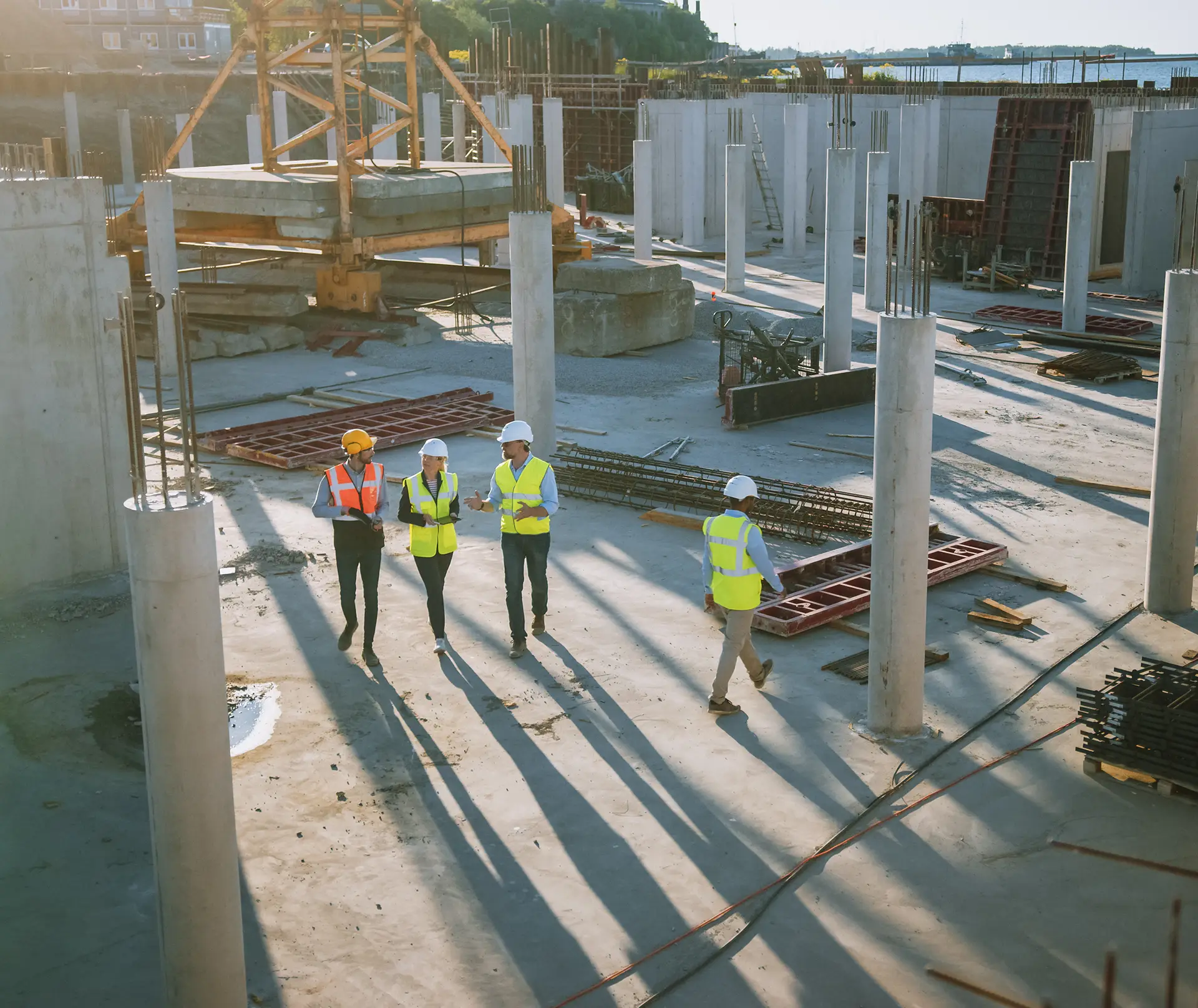 Four construction professionals in hard hats and safety vests walking through a building site