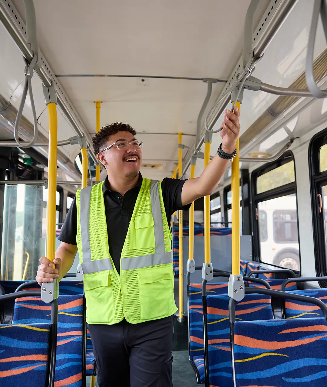 First Class Transportation employee in a safety vest holding a grab pole inside a transit bus