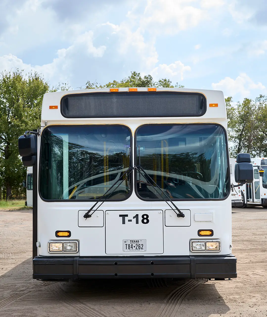 Front view of a white First Class Transportation transit bus in the company lot