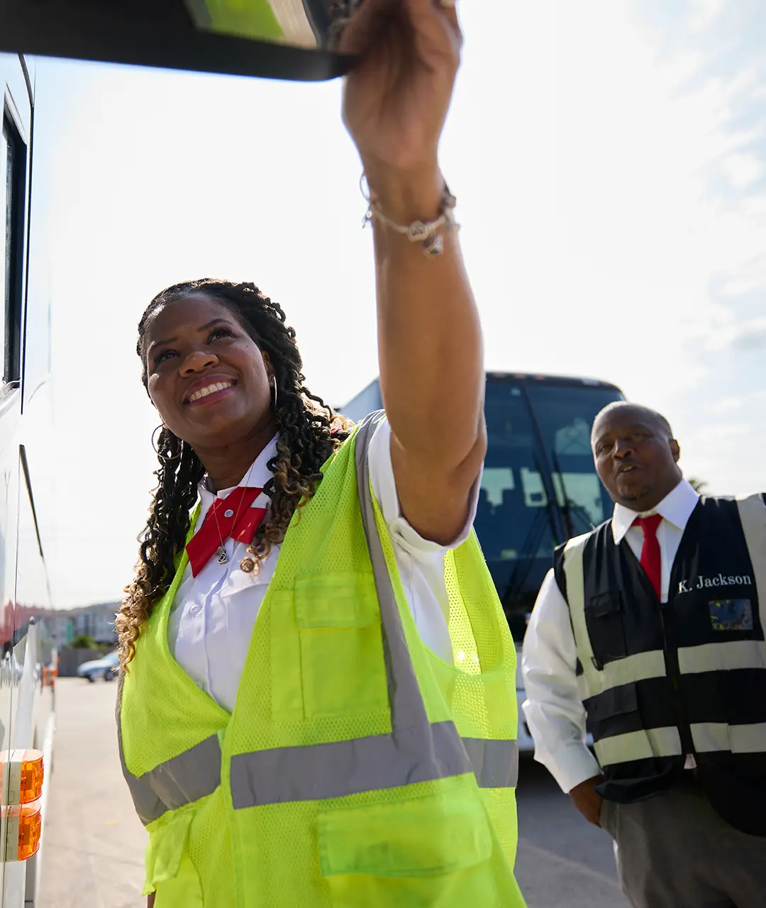 First Class Transportation employee in a safety vest adjusting the side mirror of a motorcoach