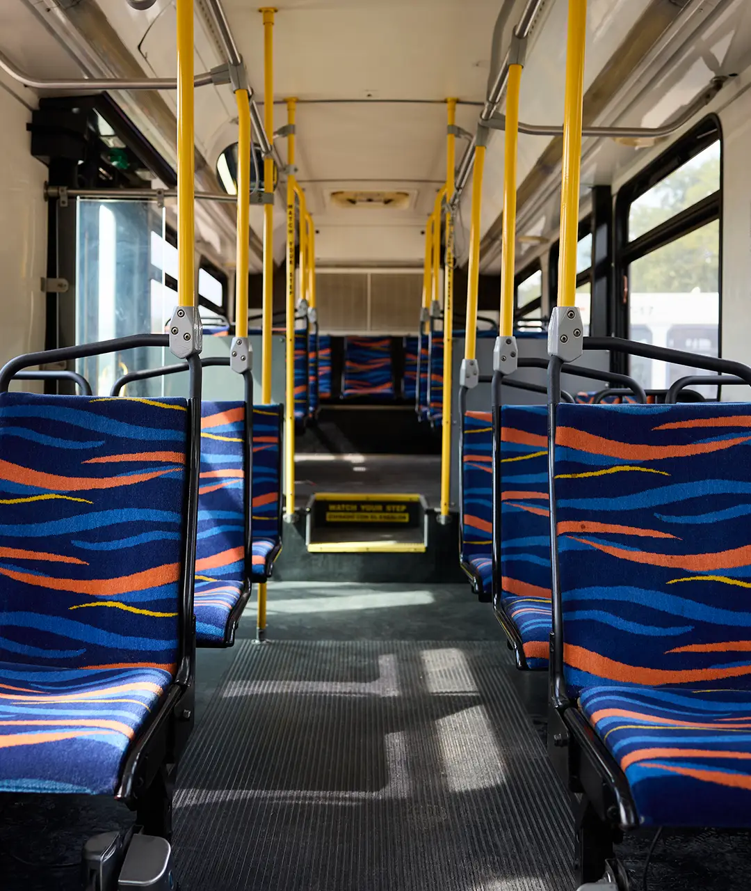 Interior of a First Class Transportation transit bus with blue patterned seats and yellow grab poles