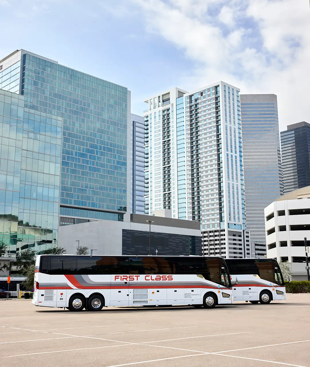 Two white First Class Transportation motorcoaches parked in a downtown Houston lot