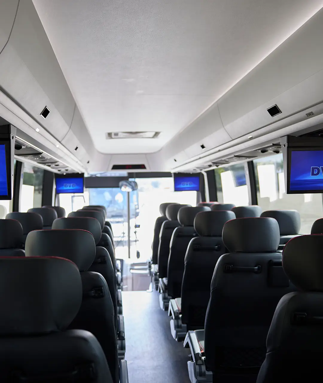 Interior aisle and seating of a First Class Transportation motorcoach with overhead DVD screens