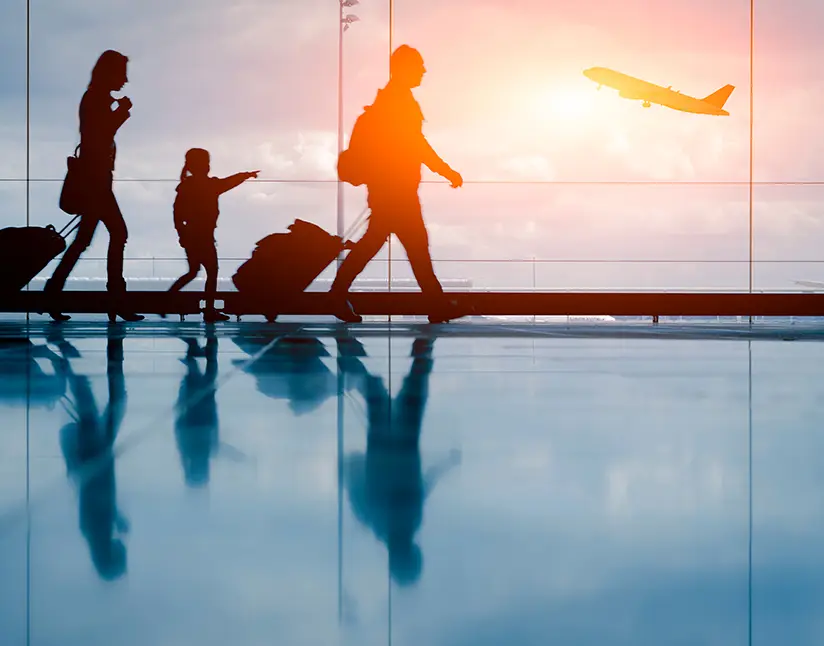 Silhouette of a family with luggage walking through an airport terminal as a plane takes off