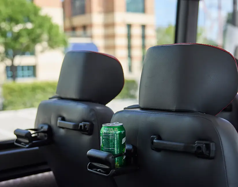 Motorcoach seatback cupholder holding a beverage can between two black leather headrests