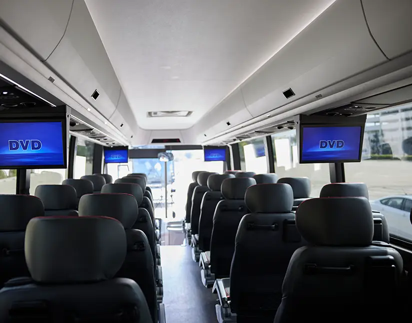 Interior of a First Class Transportation motorcoach with overhead DVD screens above rows of seats