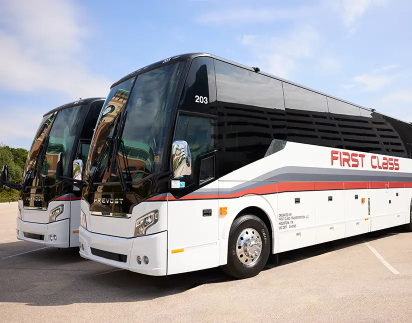 Two white First Class Transportation full-size Prevost motorcoaches parked side by side