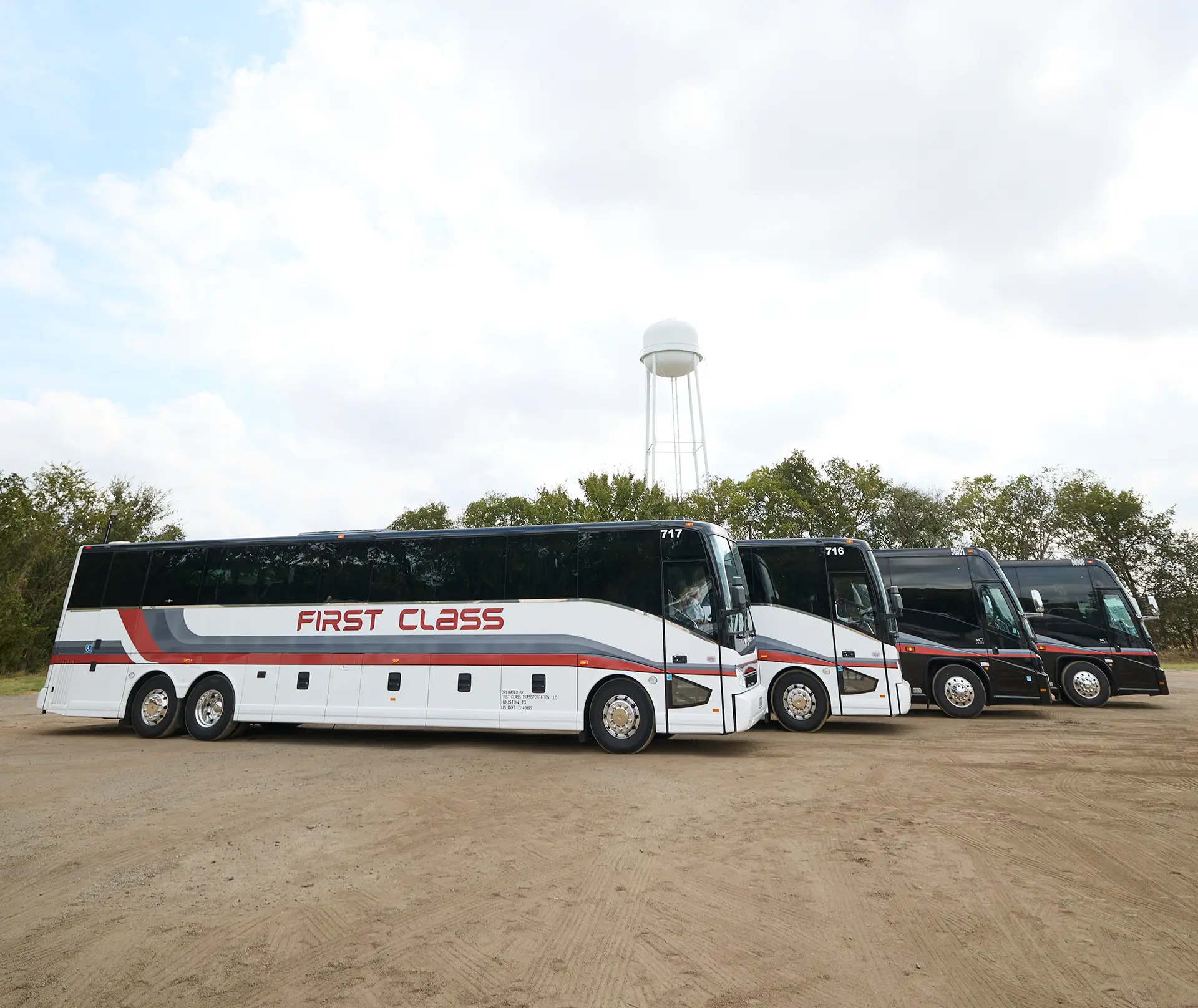 Row of First Class Transportation motorcoaches parked on a gravel lot, a white full-size coach in front of black coaches