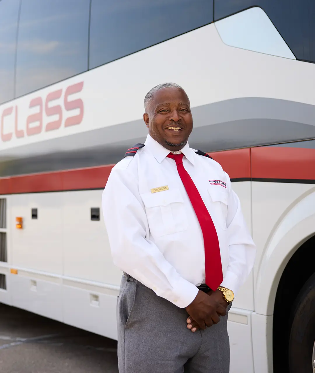 First Class Transportation driver in uniform smiling in front of a white First Class motorcoach