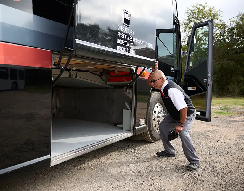 First Class Transportation driver opening the luggage bay door of a black motorcoach
