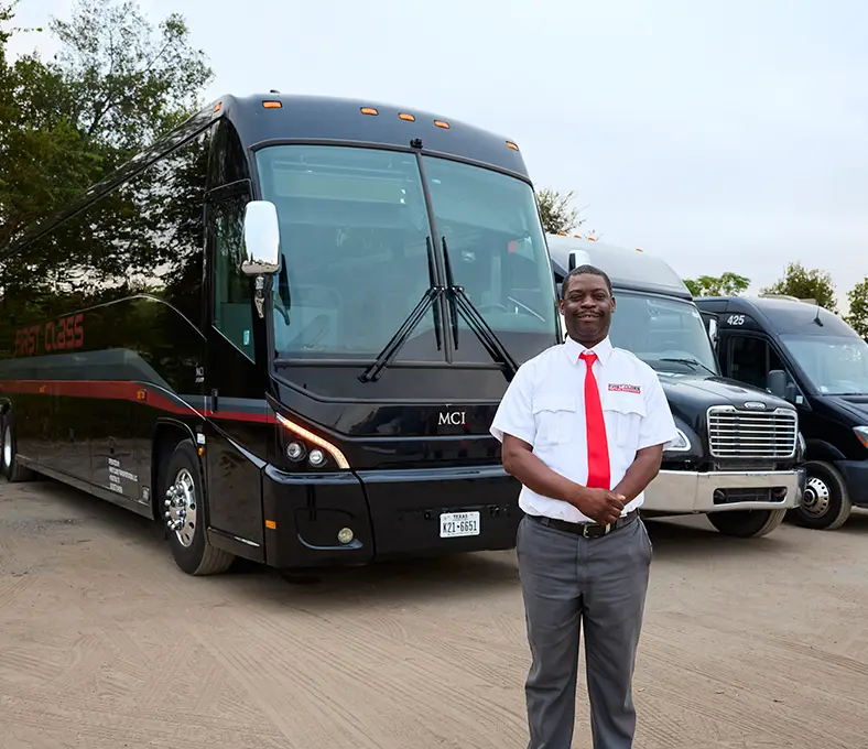 First Class Transportation driver in uniform standing in front of a black motorcoach and fleet vehicles