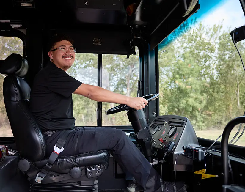 Smiling First Class Transportation driver seated at the wheel of a motorcoach