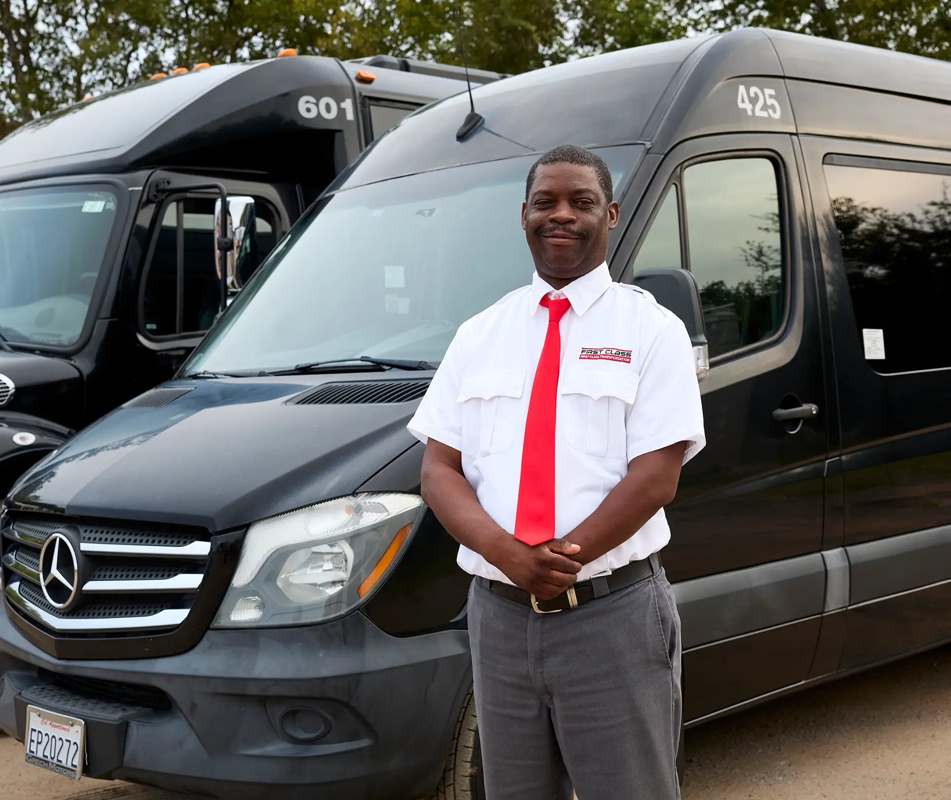 First Class Transportation driver in uniform standing beside two black Mercedes Sprinter vans