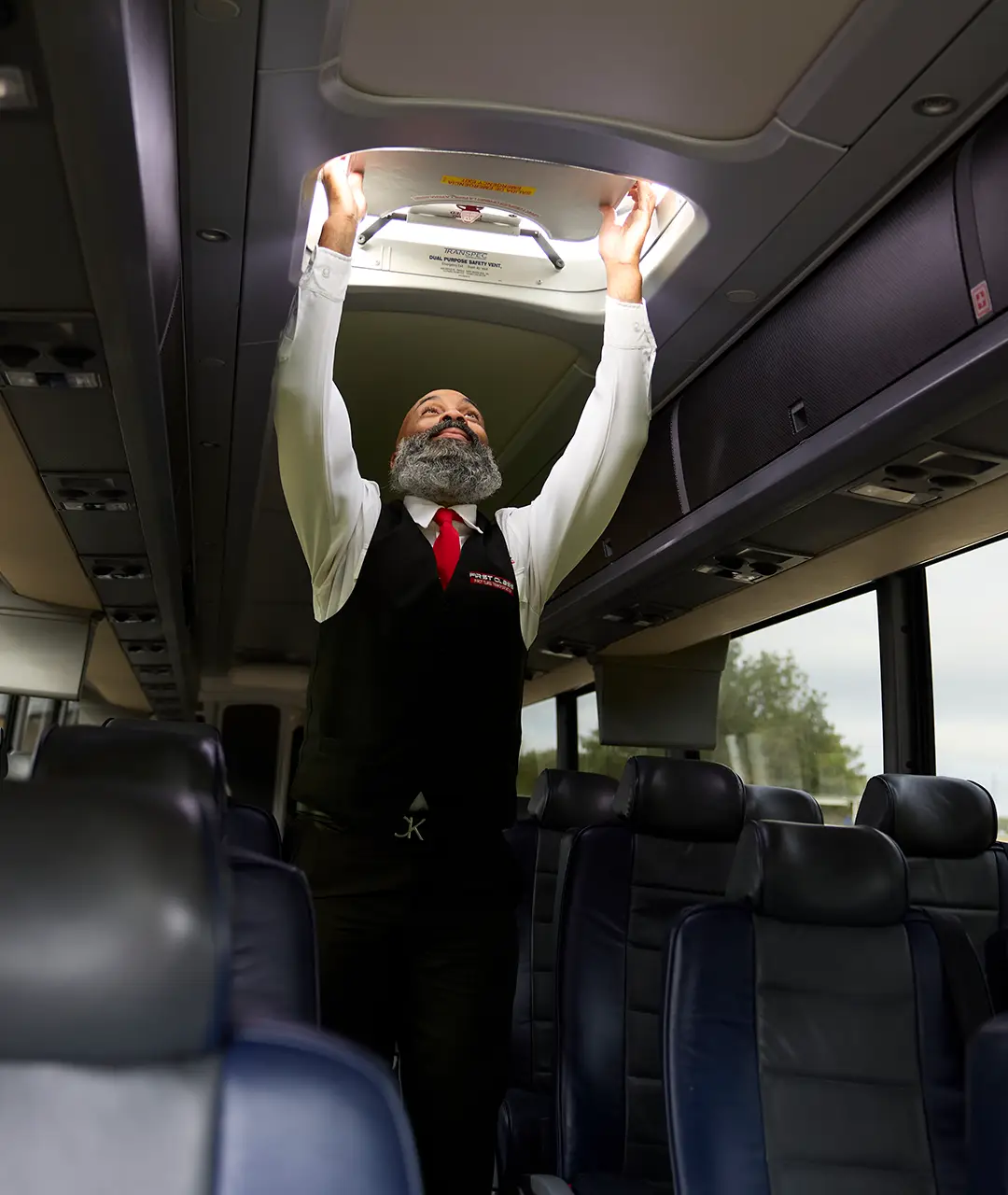 First Class Transportation driver checking an overhead safety vent inside a motorcoach