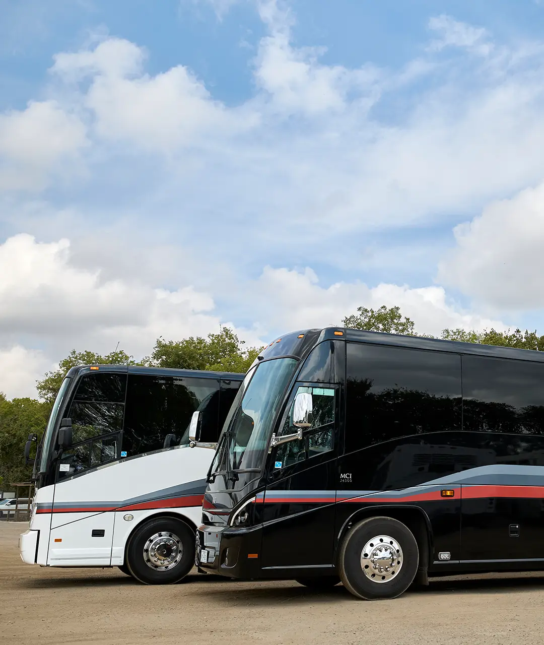 A white motorcoach and a black MCI motorcoach parked side by side at First Class Transportation