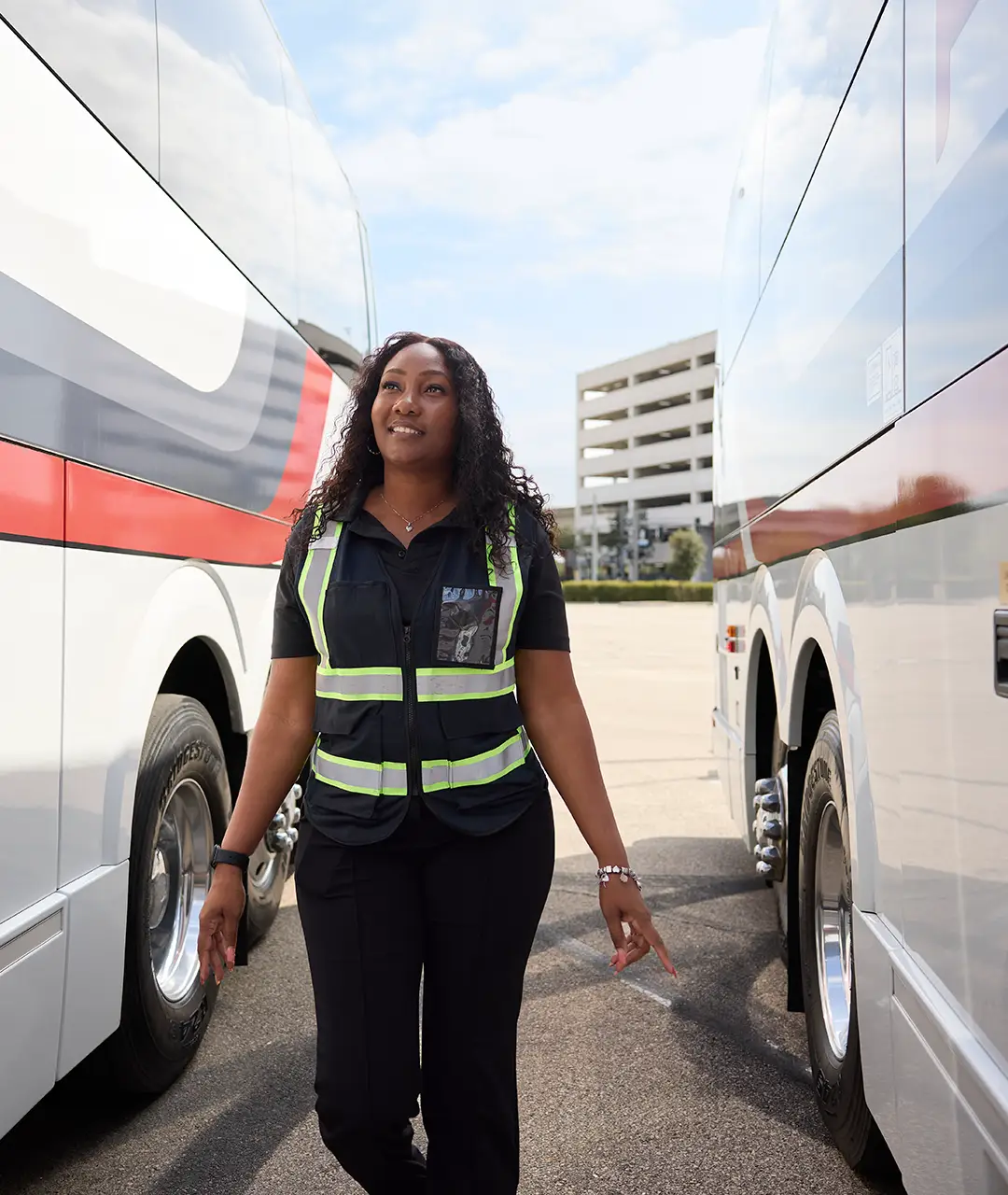 First Class Transportation employee in a hi-vis vest walking between two white Prevost motorcoaches