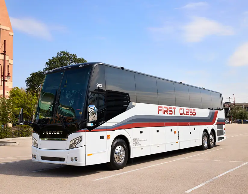 White First Class Transportation full-size Prevost motorcoach parked beside a brick building