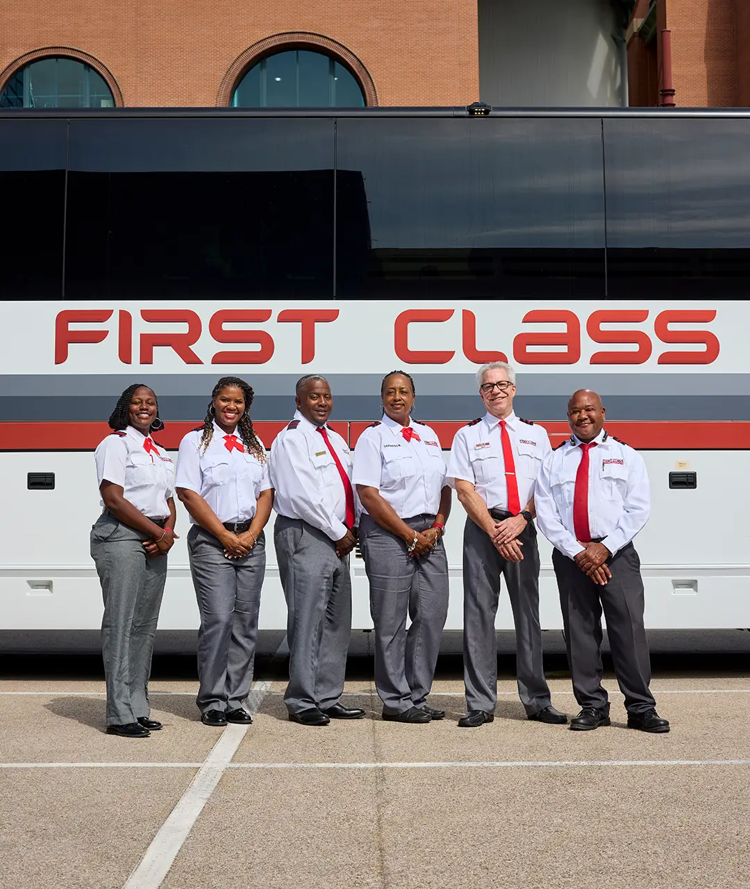 Six First Class Transportation drivers in uniform standing in front of a motorcoach
