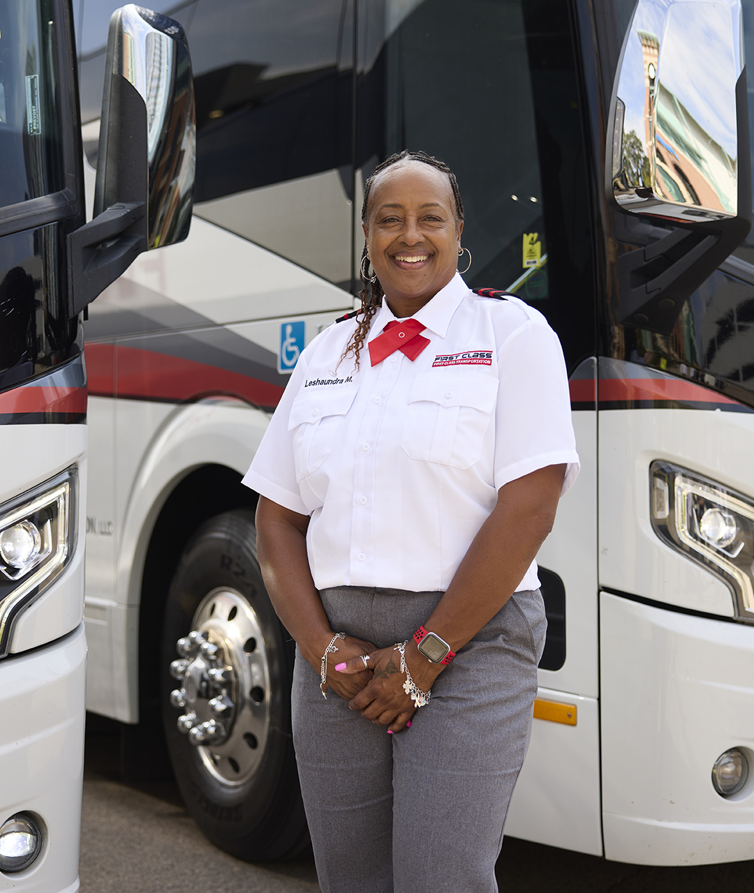 First Class Transportation driver in uniform smiling between two parked motorcoaches