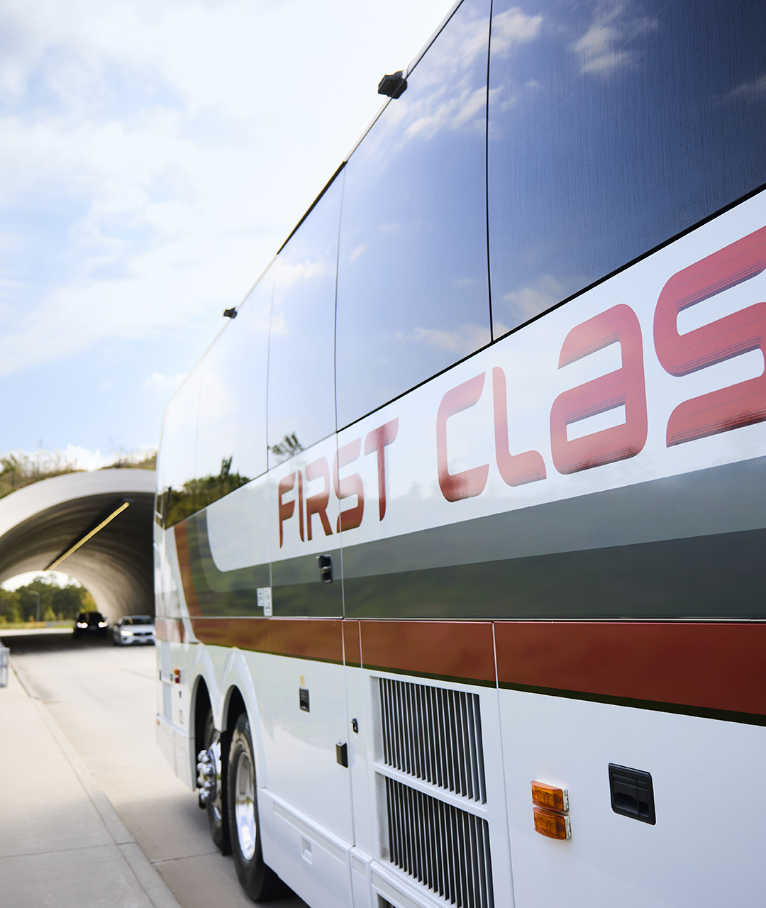Side of a First Class Transportation motorcoach passing under a highway overpass